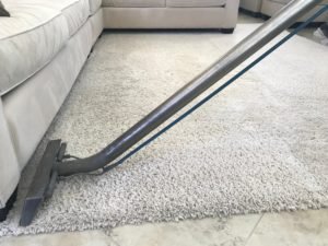 A man is using a shampooer to clean a white rug